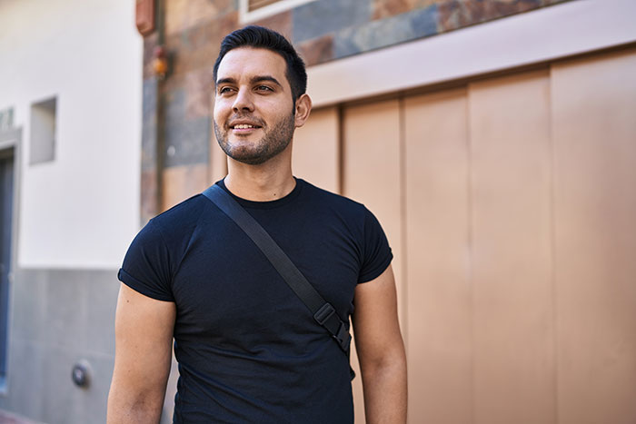 Man in a black shirt with a shoulder bag, standing outdoors and smiling, representing surprising things about men.