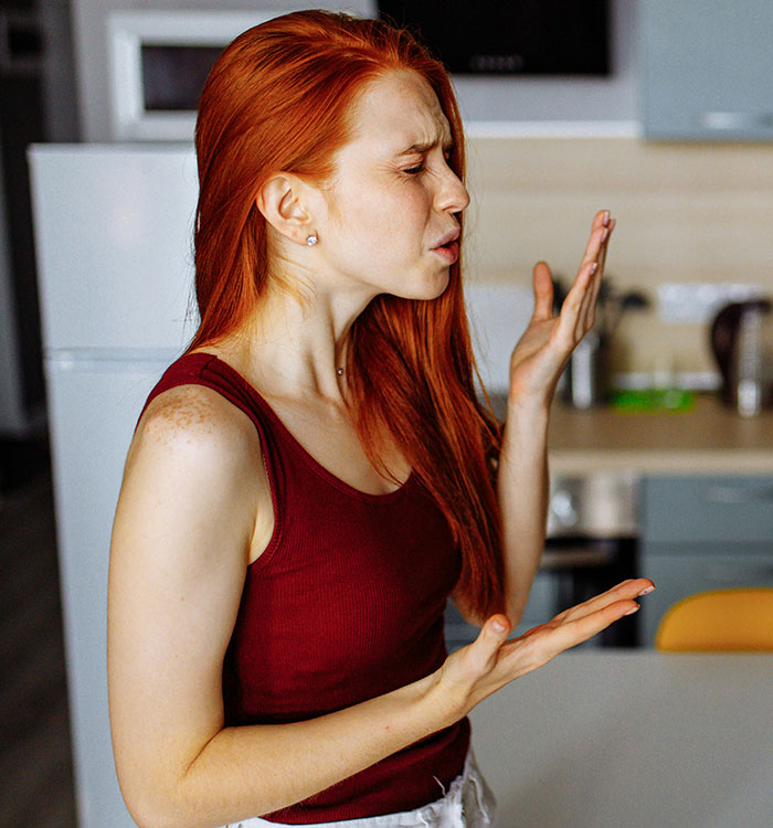 Teen prioritizing future, looking upset in kitchen, red hair, maroon top.