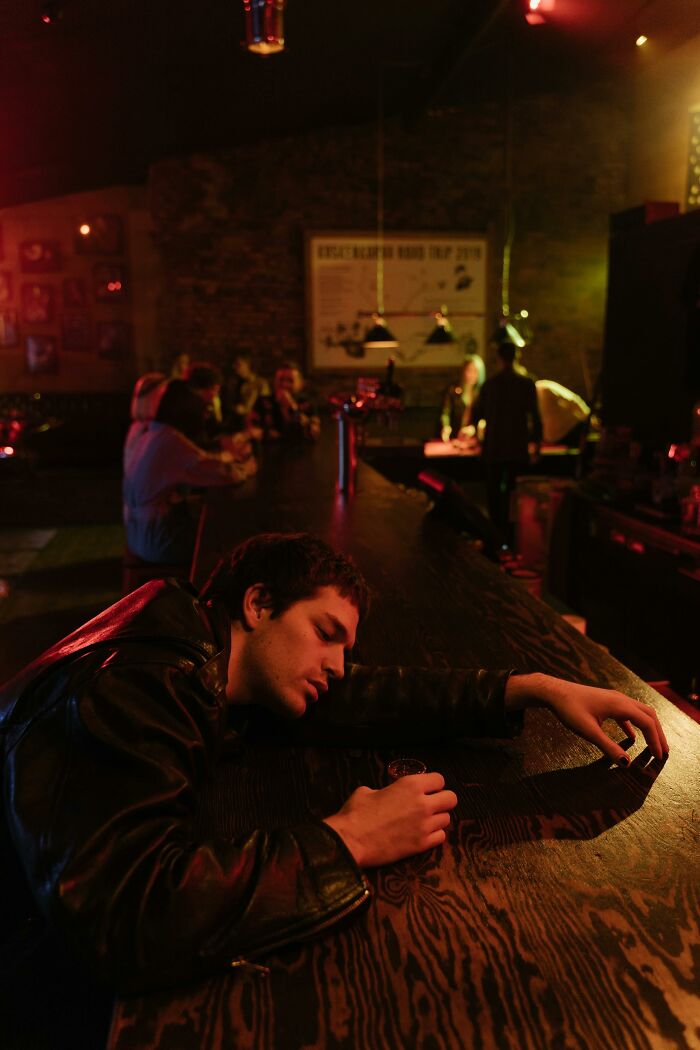 Person asleep on a bar counter with a drink, in moody lighting.