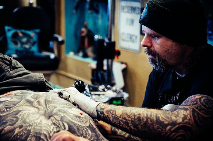 Tattoo artist creating a detailed design on a client's back in a studio setting.