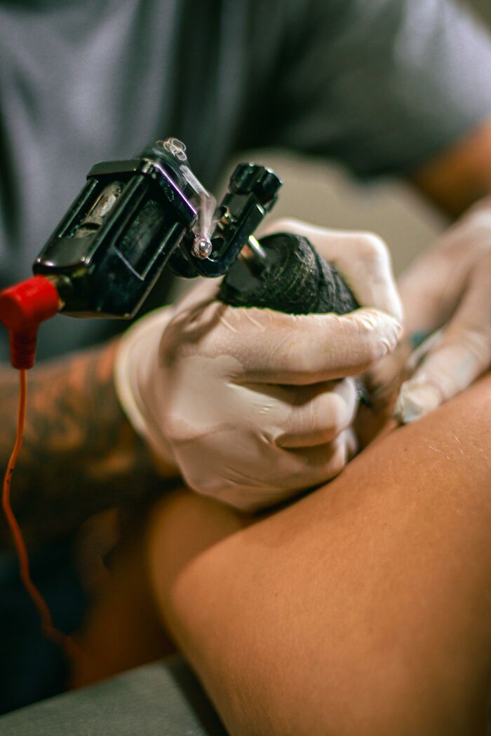 Tattoo artist working with a tattoo machine on a person's skin, focusing on intricate details.