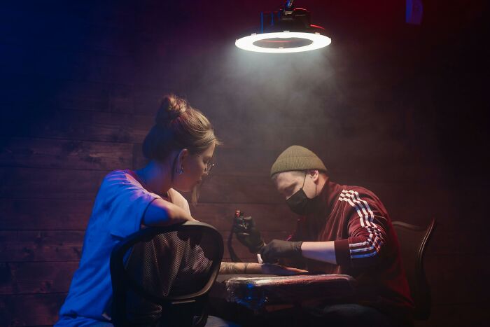Tattoo artist concentrating on a design under bright light in a dimly lit studio setting.