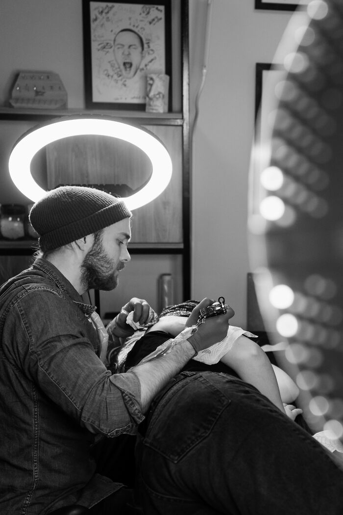 Tattoo artist concentrating on creating a design, illuminated by a halo-like light in a studio setting.