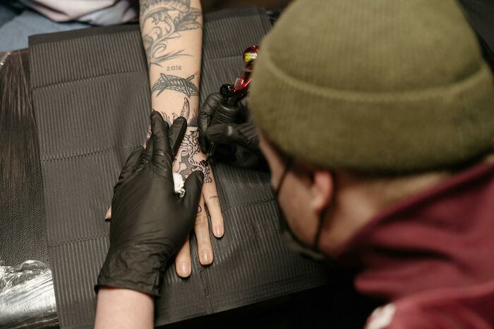 Tattoo artist wearing gloves creates detailed arm tattoo on a client.