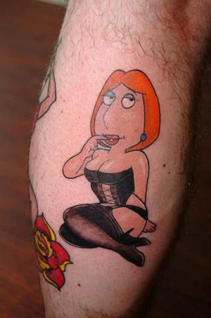 Tattoo of cartoon character in black outfit with red flower on the side, showcasing unique tattoo design by an artist.