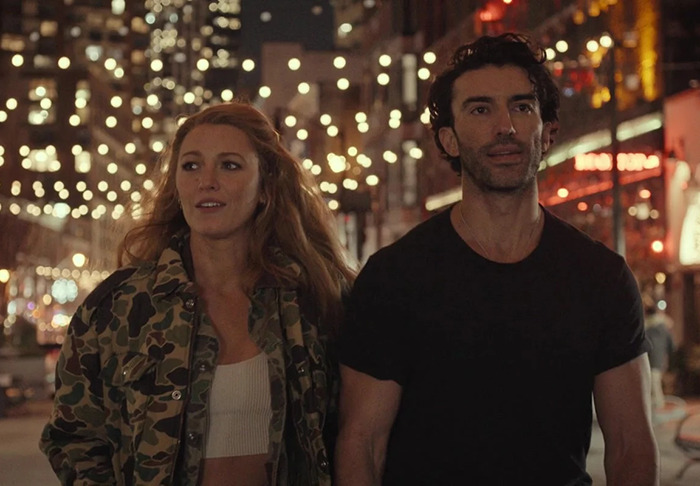 Justin Baldoni and Blake Lively walking through city lights at night, both casually dressed, and looking ahead from 'It Ends With Us'.