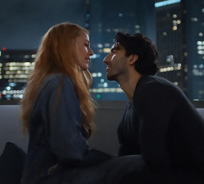Justin Baldoni and Blake Lively sitting closely on a rooftop at night with a city skyline in the background from 'It Ends With Us'.