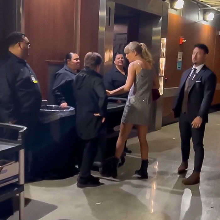 Taylor Swift in a shimmering dress gives tips to staff members backstage at the Grammys.