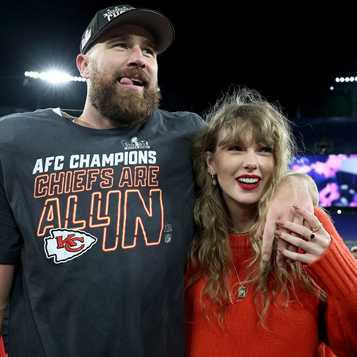 Couple laughing, one in a Chiefs shirt and the other in a red sweater, at a sports event.