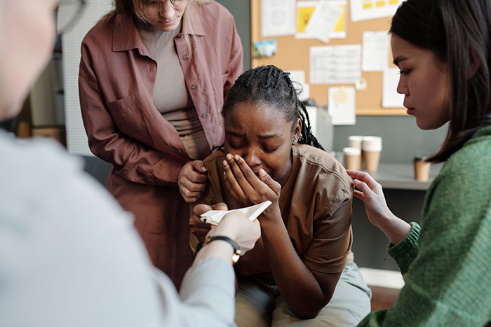 Student comforted by peers, highlighting acne-related issues and emotional support in a classroom setting.