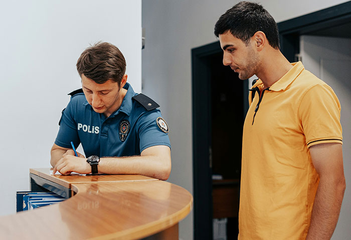 A person in a yellow shirt talks to a police officer writing at a desk, discussing a student's creepy comment. A person in a yellow shirt talks to a police officer writing at a desk, discussing a student's creepy comment.