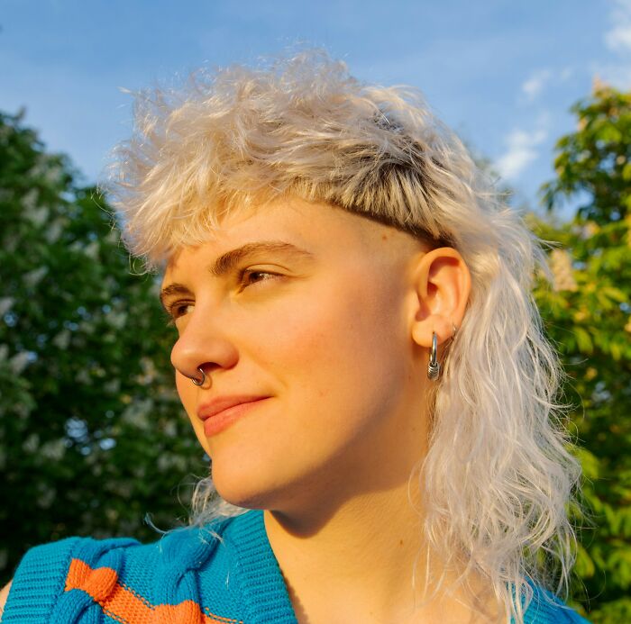 Person with a mullet hairstyle posing outdoors, showcasing recent fashion trends people hate.