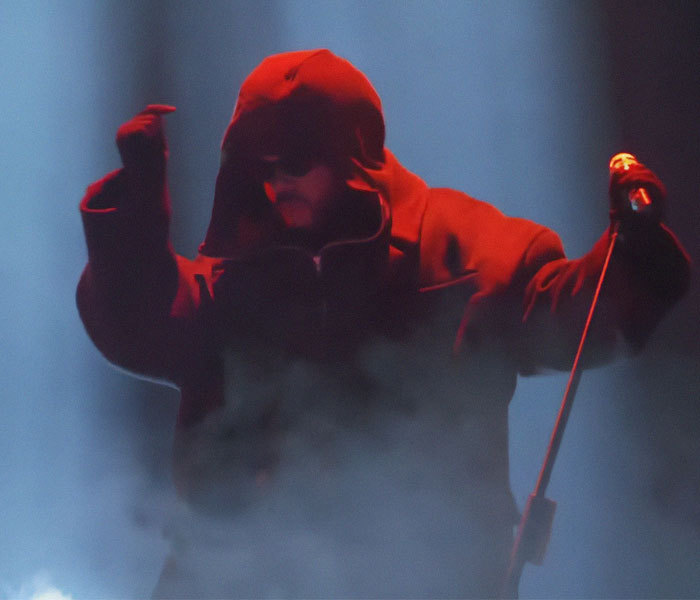 Performer in a red hooded outfit on stage, holding a microphone at the 2025 Grammy Awards, creating an awkward moment.