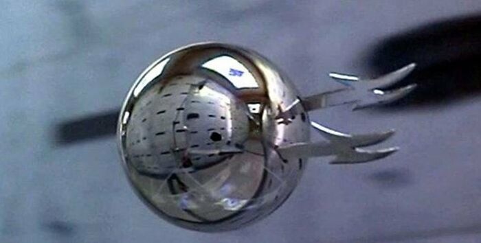 Iconic silver sphere prop from a famous movie featuring blades, reflecting a setting.