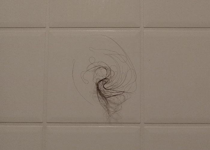 Hair swirl stuck on a bathroom tile wall, illustrating surprising things men learn in relationships with women.