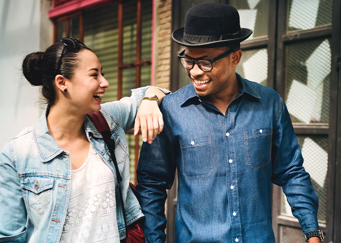 Happy couple walking outdoors, man in a hat and glasses, woman in denim jacket, representing relationship insights.