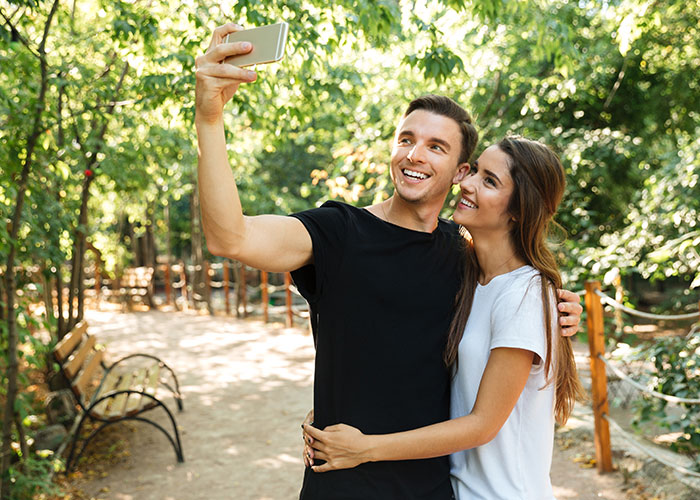 Couple taking a selfie in a park, capturing a joyful moment.