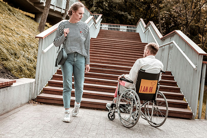 A woman walks beside a man in a wheelchair, showcasing a moment that reflects understanding grief.