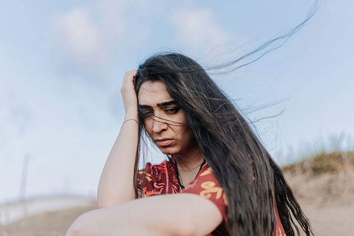 A woman sitting outdoors, looking pensive and overwhelmed, symbolizing grief and deep emotional reflection.