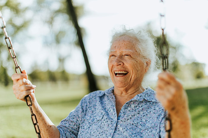 Elderly woman smiling joyfully on a swing, experiencing happiness in a park setting.