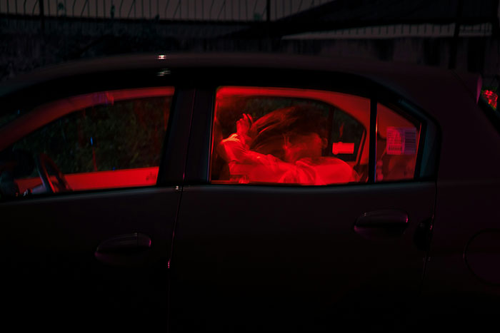 A person in a car bathed in red light, expressing grief with head in hands.