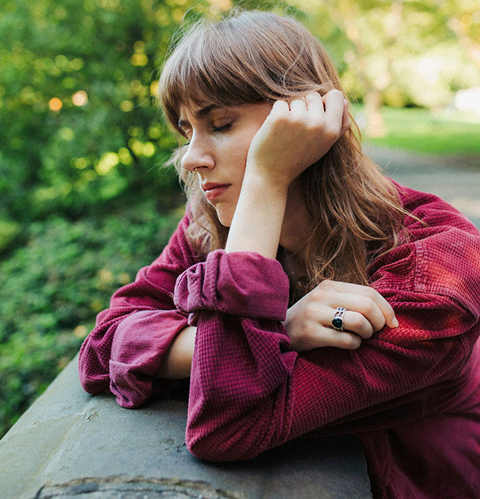 A woman in a thoughtful pose wearing a red shirt, sitting outdoors, symbolizing grief.