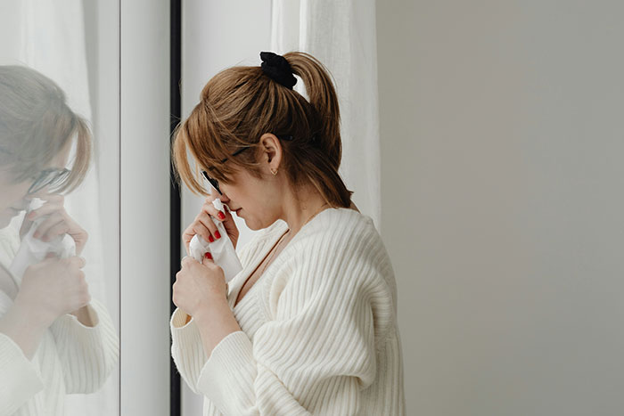 Woman in a white sweater, holding a tissue, experiencing grief near a window.