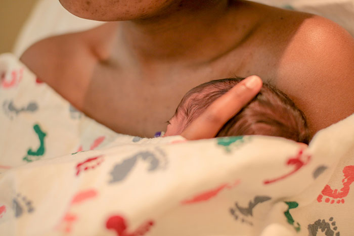 A newborn nestled in an adult's arms, wrapped in a patterned blanket, conveying vulnerability and care.