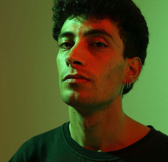 Young man with earrings in moody red and green lighting, reflecting on scary and sobering stories about ruining life.