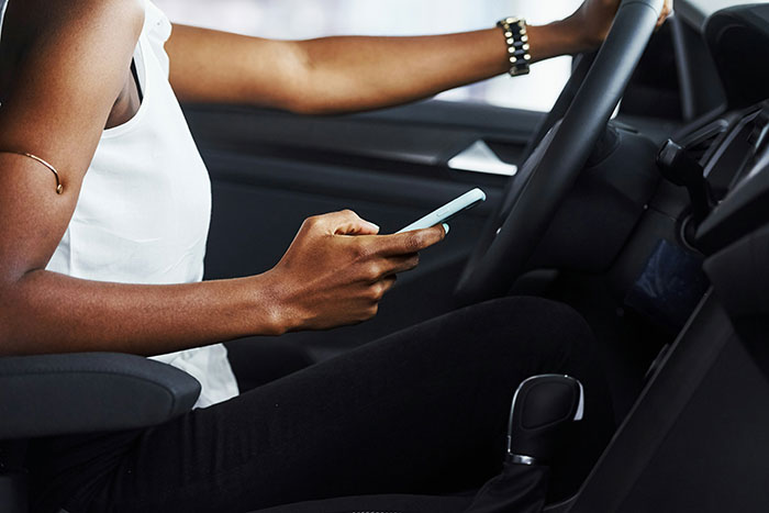 Person using a smartphone while sitting in a car, illustrating risky behavior related to how to ruin your life.