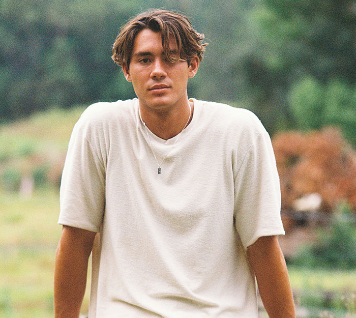 Young man outdoors wearing a beige shirt, looking thoughtful, representing stories about how to ruin your life online.