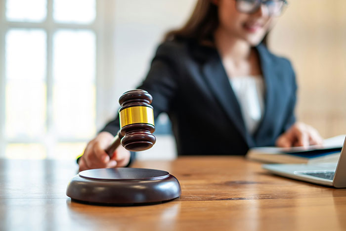 Woman in a black blazer holding a judge's gavel striking it on a wooden desk in a bright office setting