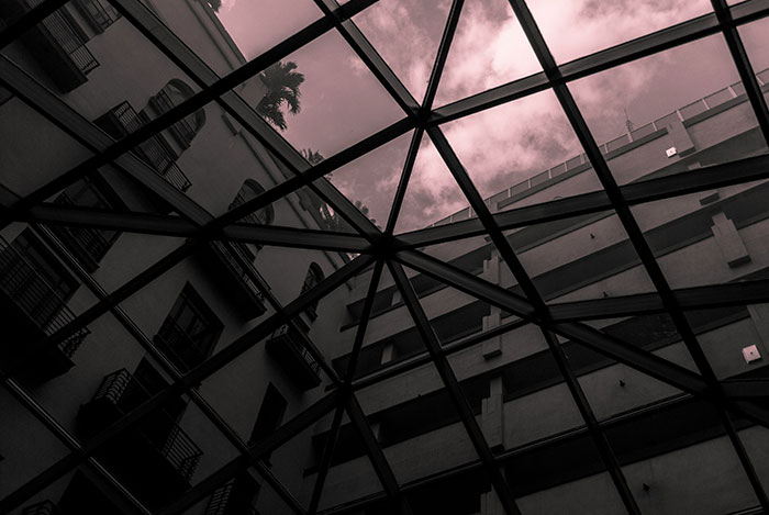 View of dark building exterior and cloudy sky through a geometric glass ceiling, evoking how to ruin your entire life theme.