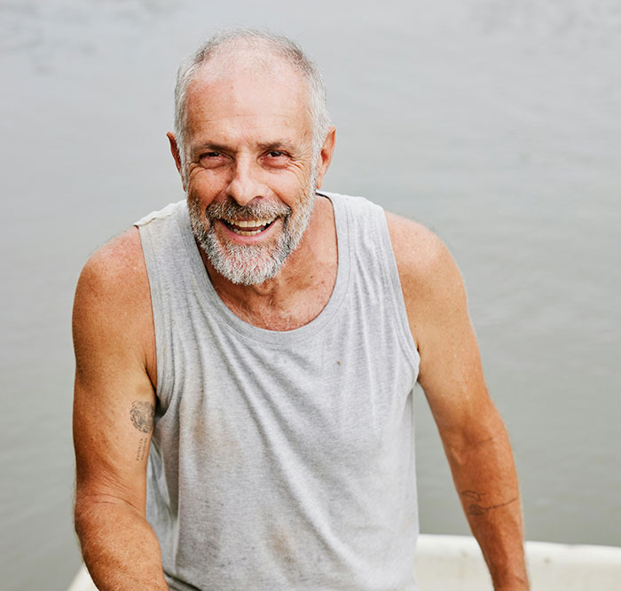 Elderly man in a gray tank top smiling by the water, representing life-changing actions.