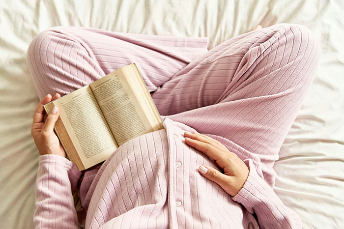 Person in pink pajamas sitting cross-legged on bed, reading a book about life lessons and personal stories.