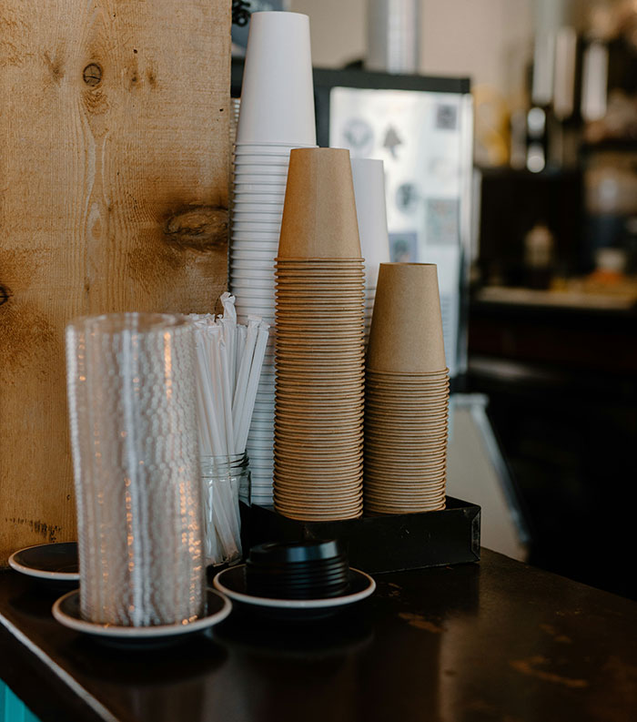 Stacks of disposable cups and straws on a counter, illustrating frugality in a minimalistic café setting.