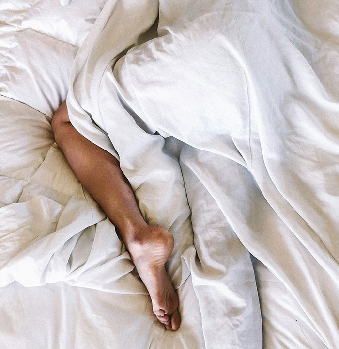 A leg peeks out from under white sheets, symbolizing frugality in minimalist living.