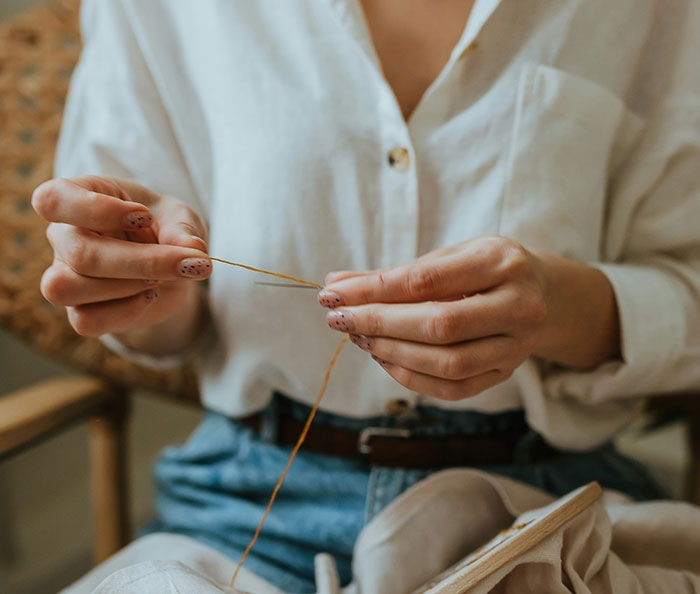 Person threading a needle, embodying frugality with a focus on DIY sewing.
