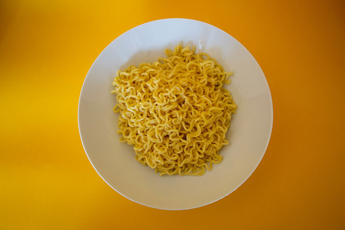 Plate of plain noodles on a yellow background, illustrating frugality in meal choices.
