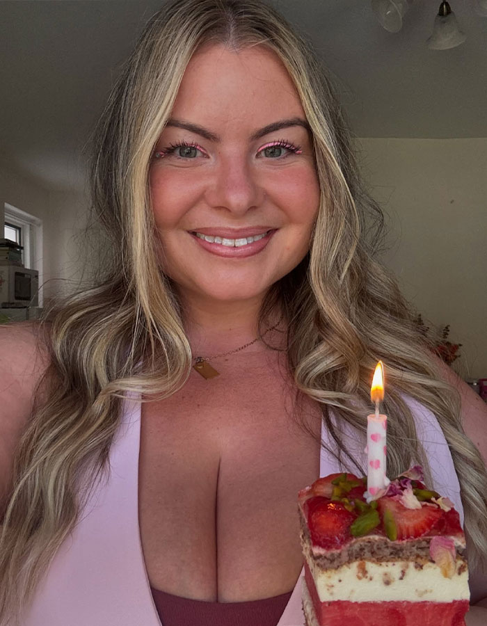 Woman smiling with a lit candle on a cake, addressing stares at her G-cup size confidently.