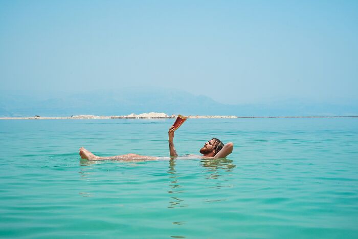Man floating in turquoise water, holding a book, illustrating natural wonders' serene beauty.