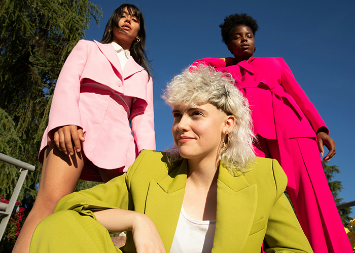 Three young women wearing colorful suits, confidently posing against a clear sky; includes prom suit fashion keywords. Three young women wearing colorful suits, confidently posing against a clear sky; includes prom suit fashion keywords.