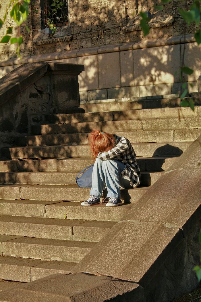 Person sitting on stairs, head down, conveying a sense of a traumatic experience.