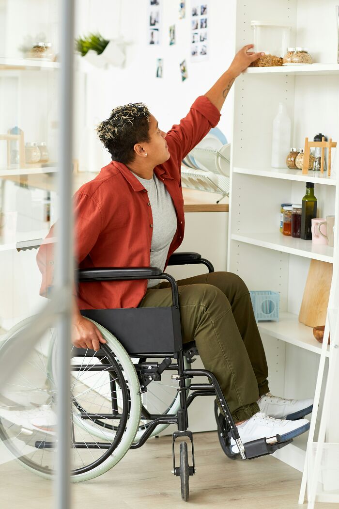 Person in wheelchair reaching for items on a high shelf, highlighting overlooked traumatizing experiences.