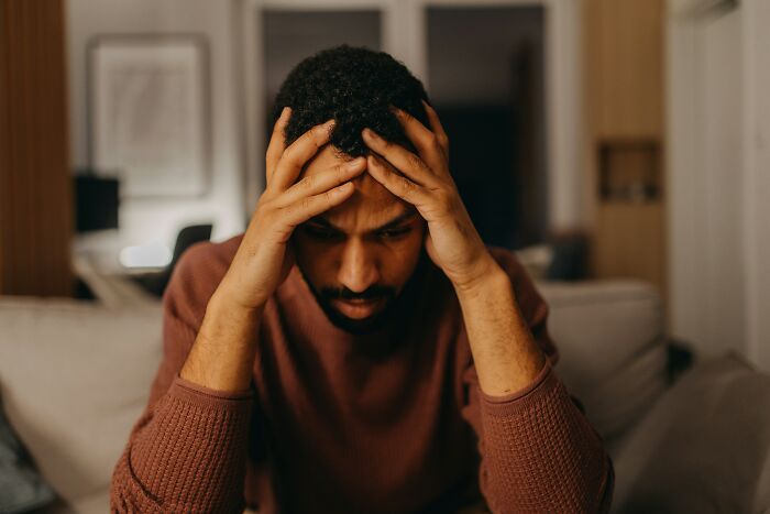 Man sitting on a couch, looking distressed, holding his head, representing traumatizing experiences.