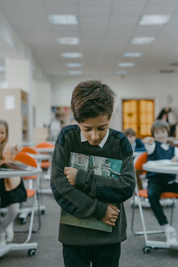 Child holding a book in a classroom setting, reflecting on traumatizing experiences not taken seriously.