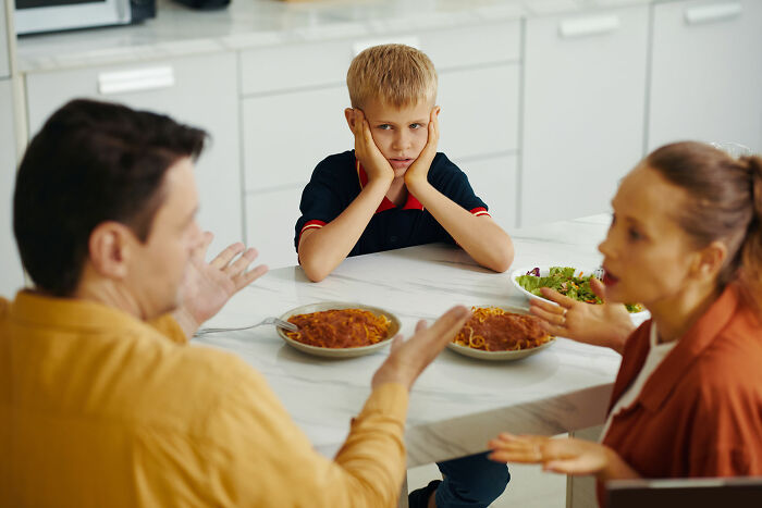 Child looks upset as parents argue at the dinner table, highlighting a traumatizing experience.