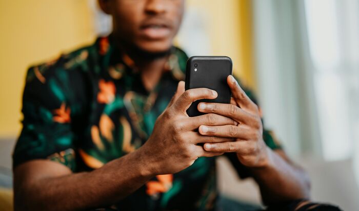 Person in a floral shirt holding a smartphone, potentially reflecting on traumatizing experiences.