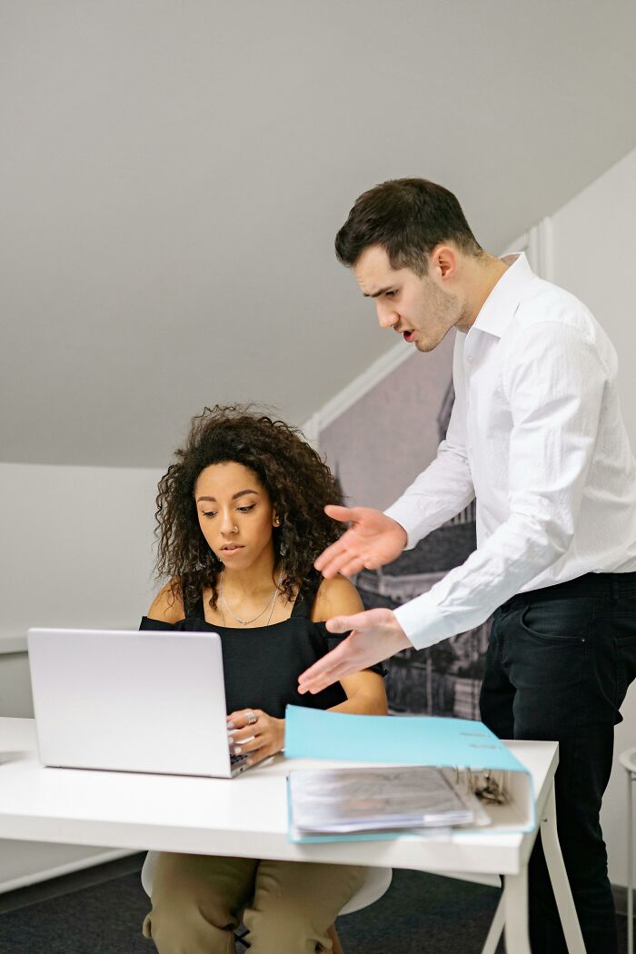 Man yelling at woman working on laptop, illustrating traumatizing experiences in a workplace.