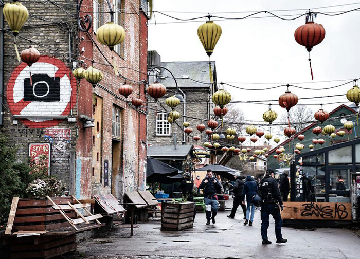 Street scene in a vibrant neighborhood with hanging lanterns and people, relating to wild questions about their homeland.